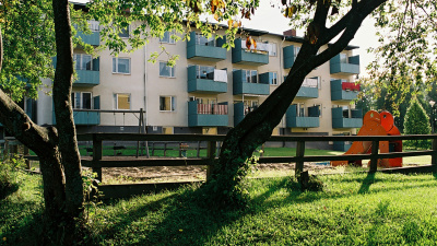 Trevåningshus i ljus puts och med blågröna balkongfronter. I förgrunden en lekplats.