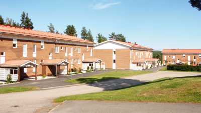 Exteriörbild av bostadsområdet Framnäs. I bilden ser man tre röda tegelhus i två våningar. Gräsmatta i förgrunden samt en asfalterad väg.