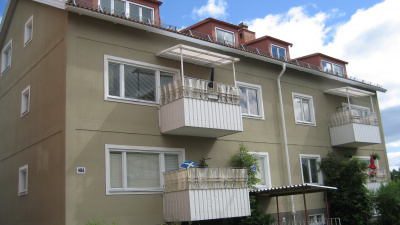 Lägenhetshus i ljus puts i tre våningar med vita balkonger.