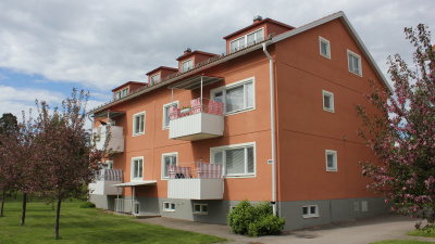 Bild på tegelrött lägenhetshus i puts med blommande körsbärsträd framför.
