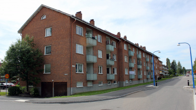 Flerbostadshus i tre våningar i rött tegel och gröna balkonger.