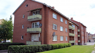 Flerbostadshus i tre våningar i rött tegel och gröna balkonger.