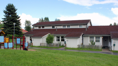 Tre ljusgråa radhus i två plan med lekplats framför.