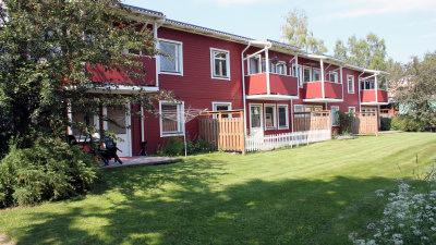 Exteriörbild av baksidan av Hambogatan 14 c-k. Flerbostadshus i två våningar med röd träfasad. Balkonger på andra våningen och uteplats i bottenplan.