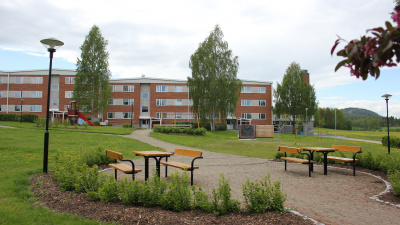 Lägenhetshus i tre våningar i bakgrunden och bänkar och bord i förgrunden.