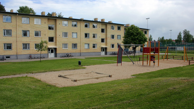 Lekplats i förgrunden och och i bakgrunden ett gult flerbostadshus i tre våningar.