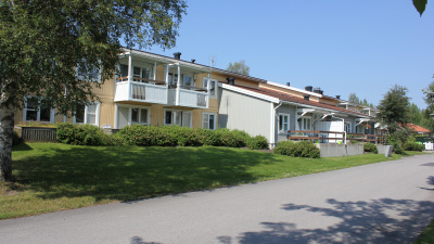 Exteriörbild av lägenheter i anslutning till Hällagården. Lägenheterna i markplan har uteplats och de på andra våningen har balkong.