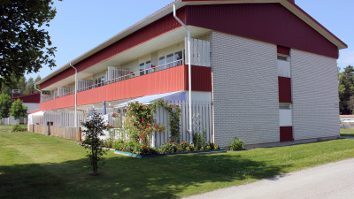 Tvåvånings flerbostadshus i tegel med grönska i förgrunden.