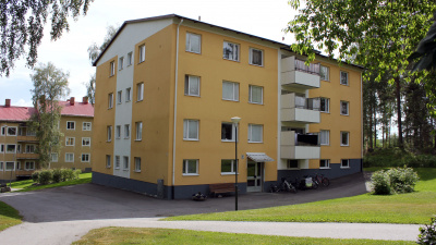 Entrésida av trevåningshus med gul putsad fasad och vita balkongfronter.