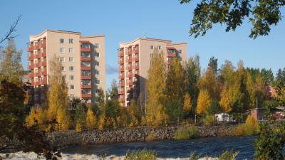 I förgrunden älven Ljusnan och träd i höstfärger. I bakgrunden flerbostadshus i sju våningar.åll med älven Ljusnan i förgrunden.