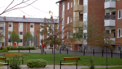 Innergård med grön gräsmatta, en parkbänk samt två flerbostadshus i tre våningar och rött tegel.