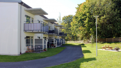 Flerbostadshus i två våningar. Uteplatser i markplan med plattor. Lägenheterna på andra våningen har balkong.