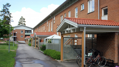Exteriörbild av entrésida av lägenhetshus i två våningar. Fasad i rött tegel och små tak över entréerna.
