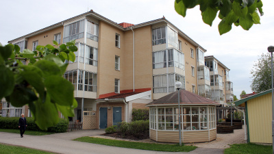 Flerbostadshus i fyra våningar med inglasade balkonger och uteplatser i markplan. Framför huset står ett lusthus.