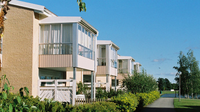 Lägenhetshus i två våningar med inglasade balkonger på våning två och uteplatser i markplan.