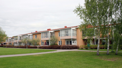 Översiktsbild av innergård av flrerbostadshus i två våningar. Inglasade balkonger på våning två och uteplatser i markplan. Gräsmattor och buskar framför huset.