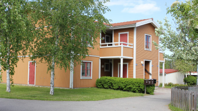 Översikt av innergård på bostadsområdet Örsängesvägen. Tvåvånings flerbostadshus med träfasad. Egna ingångar där lägenheterna på andra våningen nås via loftgång.