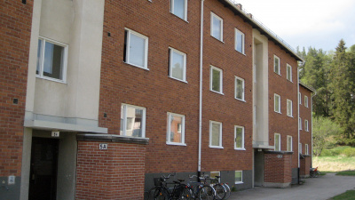 Entréer på Södra Bäckvägen. Flerbostadshus i tre våningar i rött tegel med ljusa partier. Cyklar parkerade vid entén.