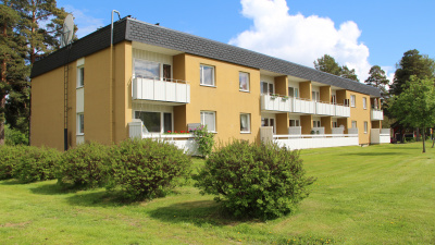Flerbostadshus på Skolmästaren i Arbrå. Exteriörbild på ett gult hus i två plan med svart takfot. Bilden visar baksidan med vita balkongräcken.