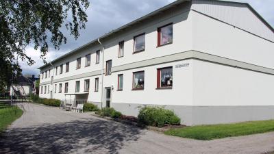 Flerbostadshus med grusad innergård. Hängbjörk med löv i förgrunden.