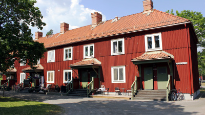 Lägenhetshus i två våningar med röd träfasad. Liten trapp leder upp till entrédörrarna som har litet tak över sig.