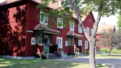 Flerbostadshus med röd träfasad. En liten trapp upp till entrédörren som har ett litet tak över sig. Ett stort träd står framför huset.