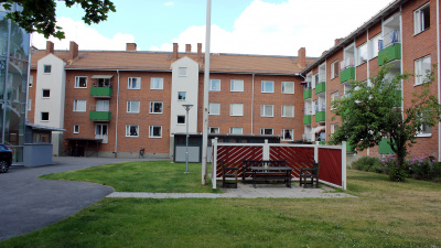 Översikt av innergård med gröna gräsmattor, flaggstång och trädgårdmöbler. Innergården omsluts av flerbostadshus i tre våningar i rött tegel och gröna balkonger.