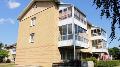 Flerbostadshus i tre våningar i ljust tegel. Bilden visar baksidan. Lägenheter i markplan har uteplats och lägenheter på våning två och tre har inglasade balkonger.