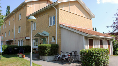 Flerbostadshus i två och tre våningar i ljust tegel. Gavellägenhet har egen ingång med gröna häckar som omsluter entrén. Cyklar är parkerade i ett cykelställ.