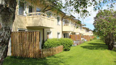 Exteriörbild av baksida av Videt. Uteplatser i markplan och balkonger på andra våningen. Huset är gult med svart plåttak. Uteplatserna omges av staket med gräsmatta utanför.