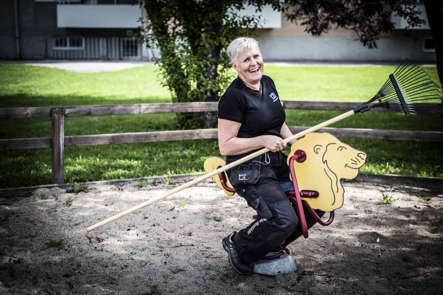 Glad fastighetsskötare som sitter på en gunghäst i en lekpark