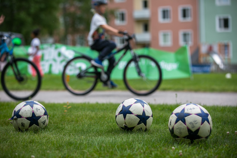 Bild på två fotbollar i förgrunden och ett barn på cykel i bakgrunden