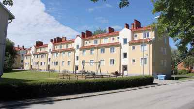 Flerbostadshus i tre våningar i gul puts. Lekpark och gröna buskar i förgrunden.