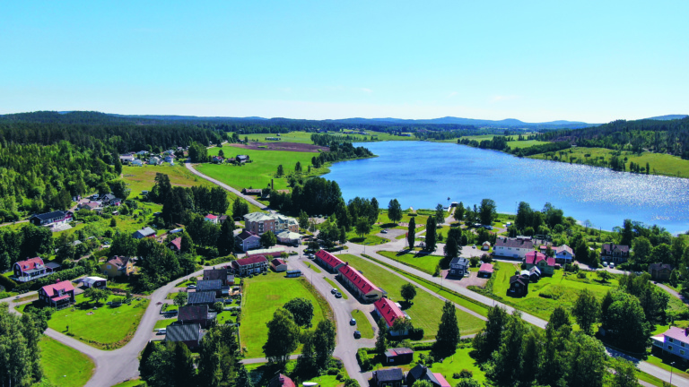 Flygbild över Rengsjö med bebyggelse, grönska och sjön i bakgrunden.